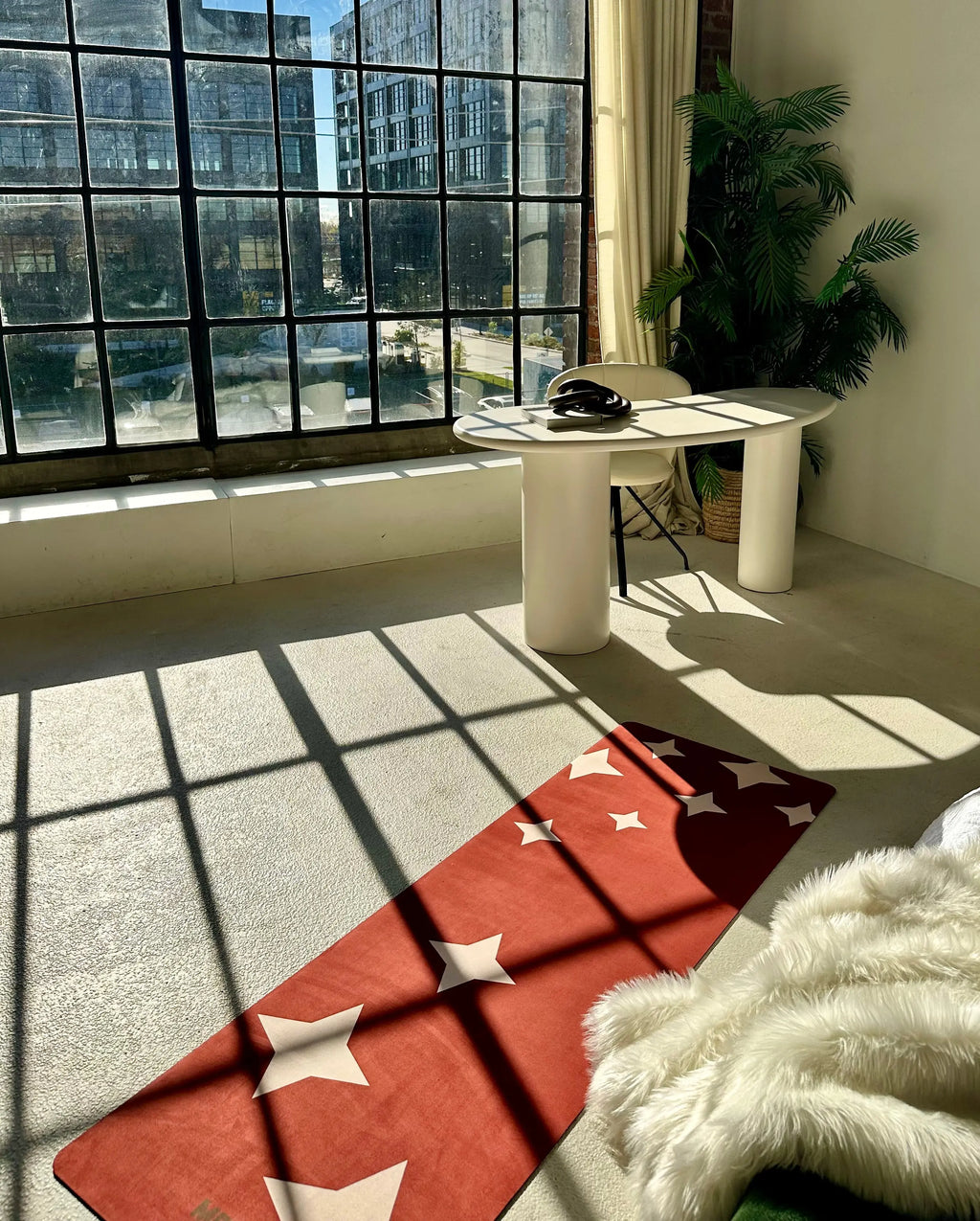 Modern room with a large window, white table, and red yoga mat with star patterns.