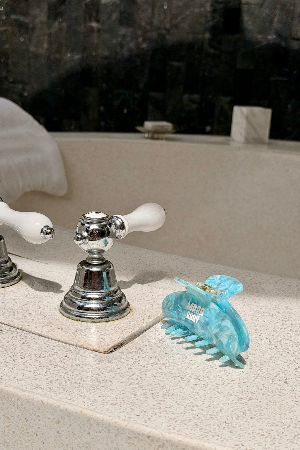 A translucent light blue hair claw clip resting on a speckled beige bathroom sink countertop next to a chrome faucet.