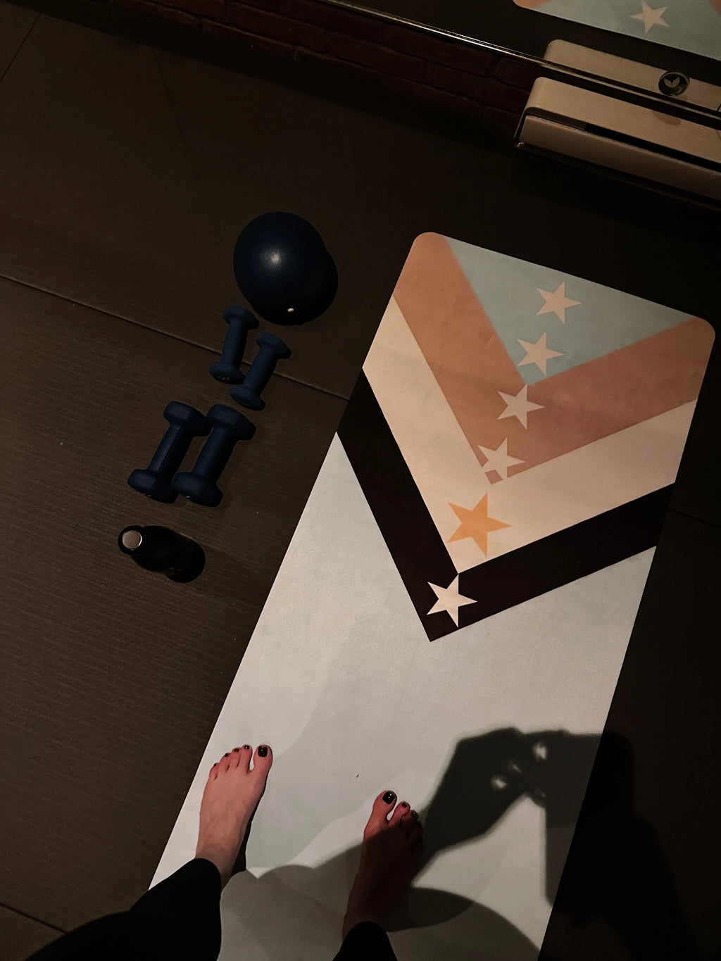 Yoga mat with star pattern on a dark floor, next to dumbbells and a pilates ball in hot yoga and hot pilates studio